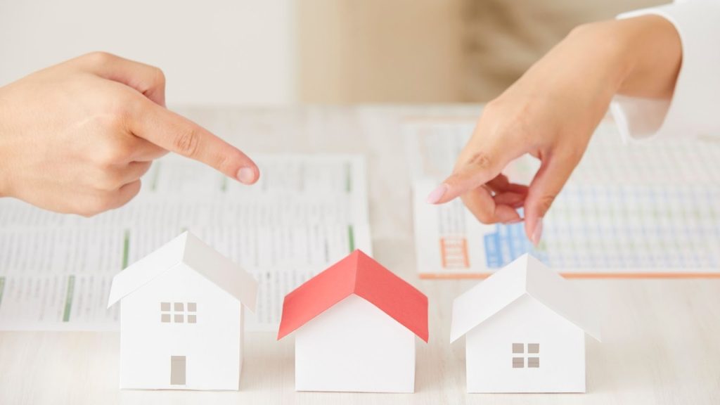 Two fingers pointing at small model houses, representing buying homes in Kathmandu.