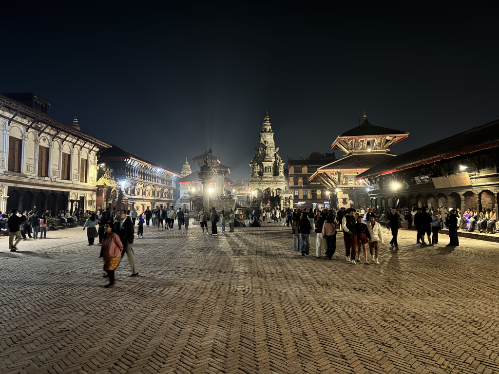 Bhaktapur Durbar Square at night with illuminated temples and people walking on brick streets